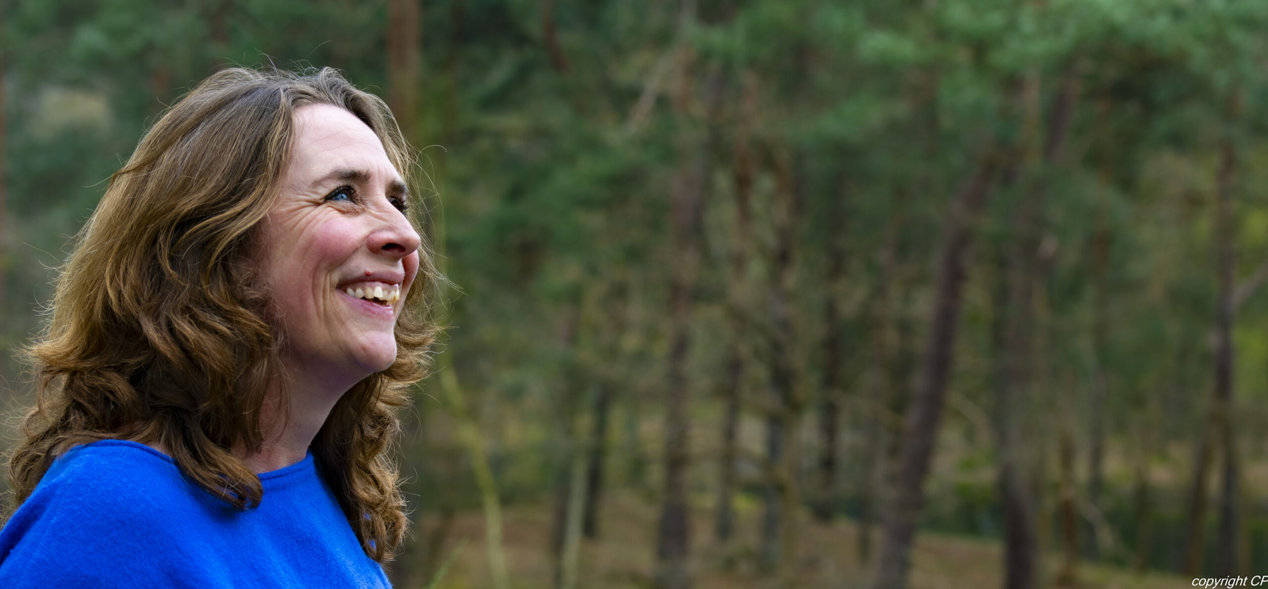 Foto van lachende Adriënne Naron die in het bos naar de lucht kijkt