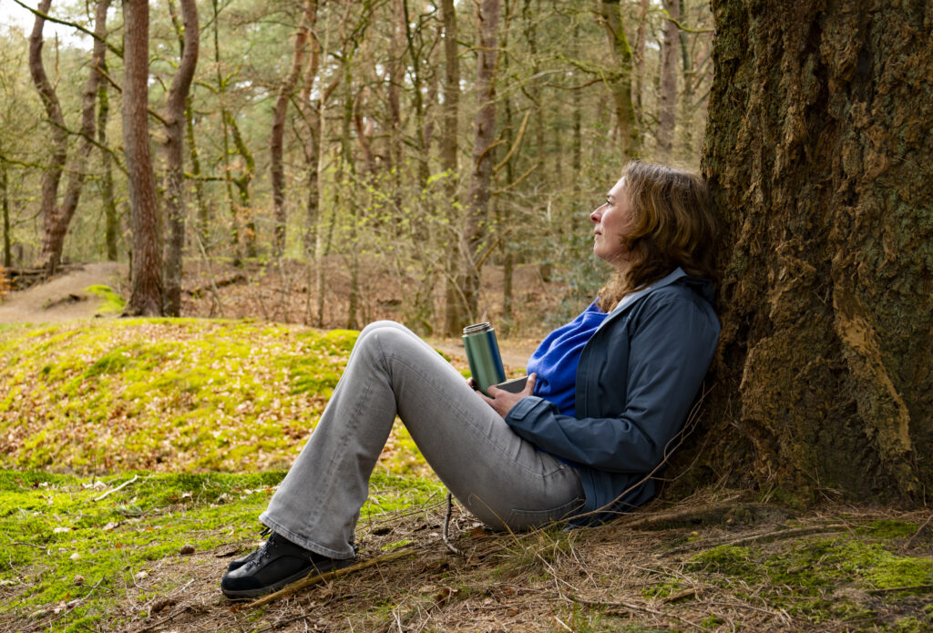 Foto van Adriënne Naron die in het bos op de grond zit, leunend tegen een boom